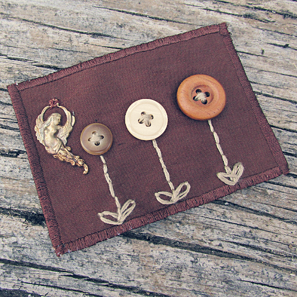brown silk ACEO with three button flowers and a brass fairy charm