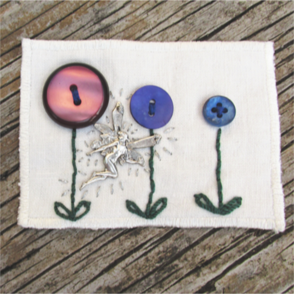 white linen ATC with blue and purple button flowers and a silver fairy
