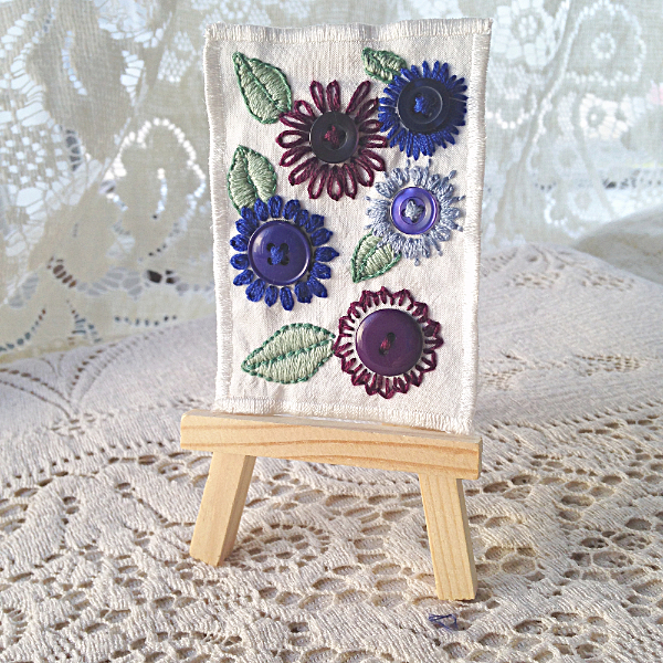 white linen ACEO with button flowers in shades of blue and purple