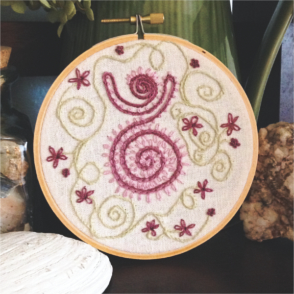 pink spiral goddess with green spirals and flowers embroidered on a cream hued muslin background