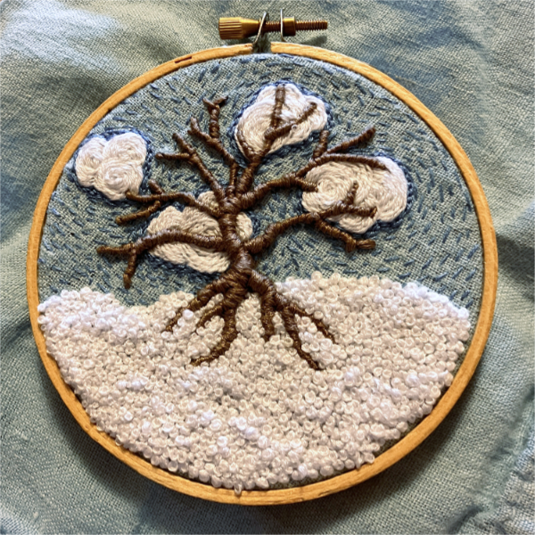 embroidered bare tree on a blue background with white clouds and white snow