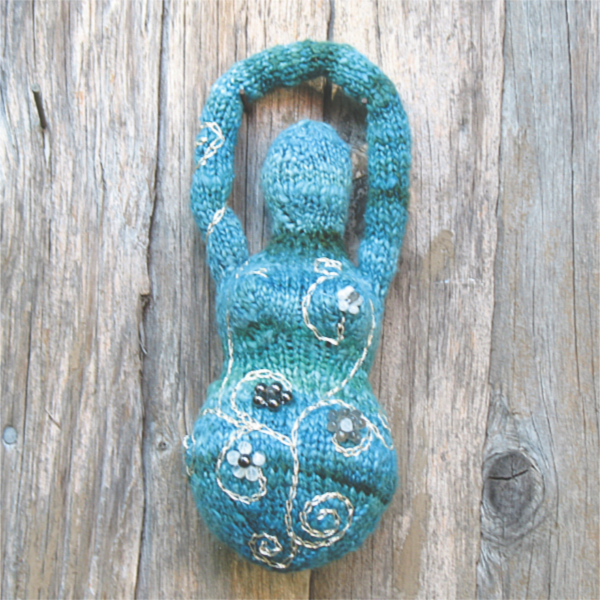 a knitted goddess in shades of aqua with beaded flowers and embroidered spirals