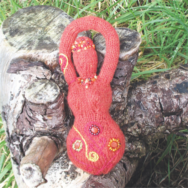 an orange knitted goddess with embroidered spirals and beaded flowers