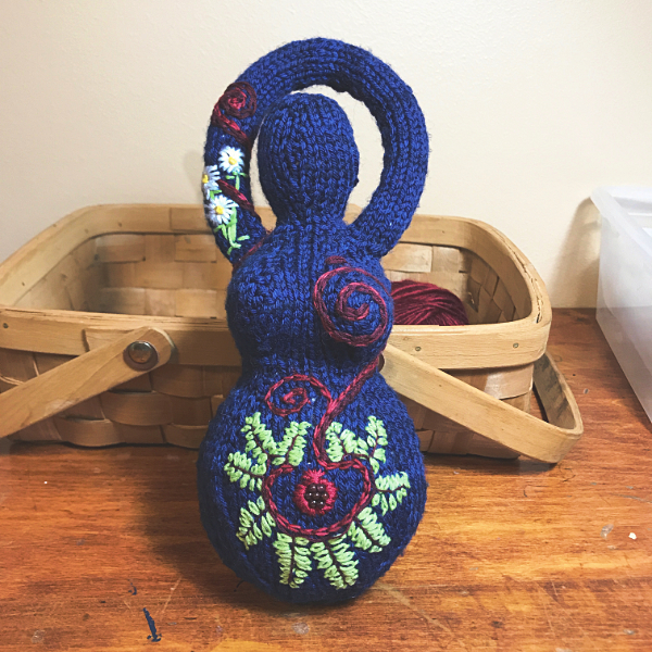 deep blue knitted goddess embroidered with ferns, a pomegranate, and daisies