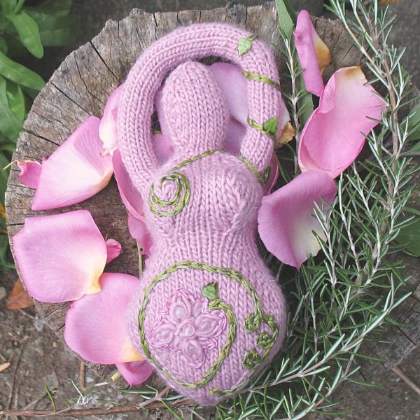 a pink knitted goddess embellished with green spirals and a pink beaded flowers