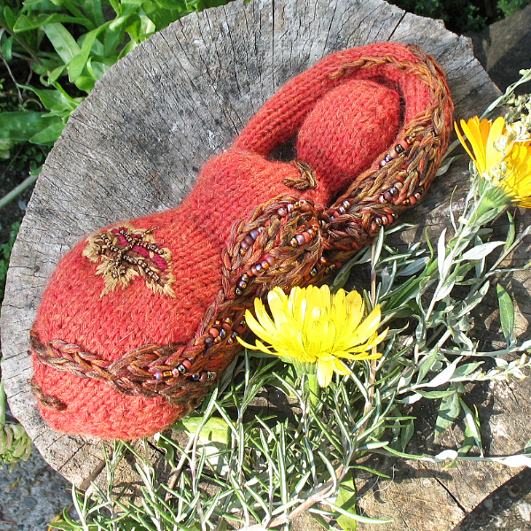 an orange knitted goddess decorated with an embroidered and beaded tree and leaf