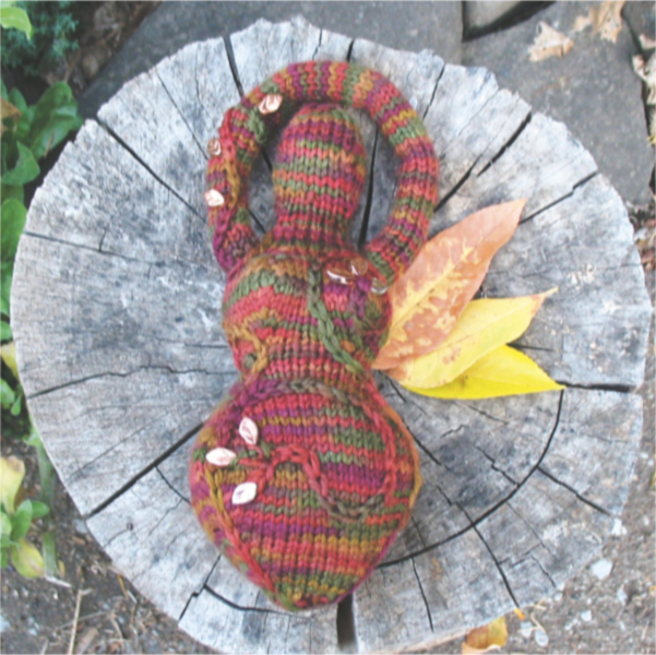 a knitted goddess in shades of orange, brown, and green, embellished with embroidery and beads