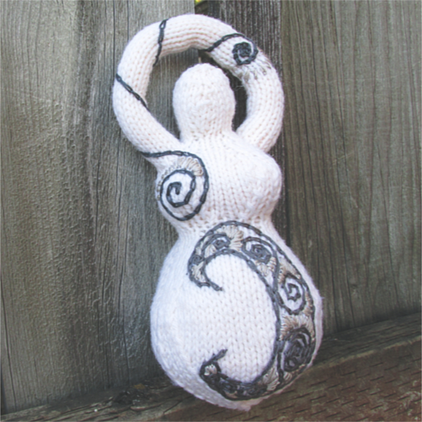 a white knitted goddess with an embroidered moon and spirals