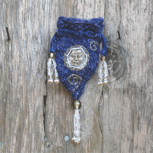 small royal blue knitted pouch with a silver moon face charm, silver embroidered spirals, and tassels made of clear beads and small bells