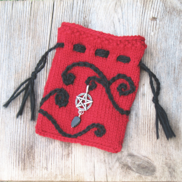 small red knitted drawstring pouch with black embroidered spirals and a silver pentacle charm