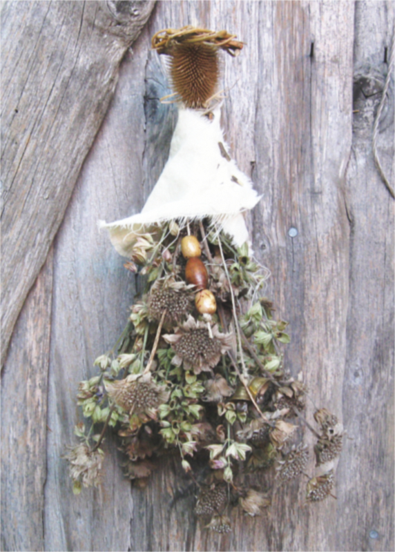 spirit doll made of dried herbs and teasel, crowned with a miniature willow leaf, wearing a white shawl held closed with a thorn