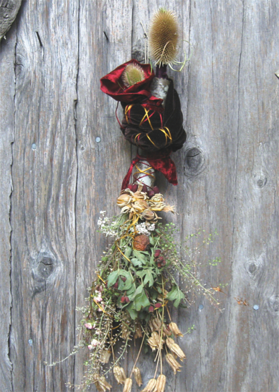 spirit doll made of dried flowers and herbs with a teasel head, wearing deep red velvet, holding a smaller spirit doll like a baby