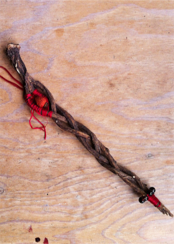 long, thin spirit doll made of braided dandelion roots, wrapped with red thread, adorned with a rose hip and garnet beads