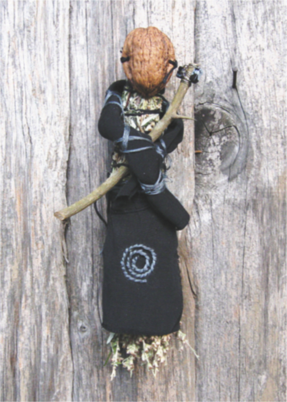 small spirit doll made of dried mugwort with a half walnut shell for a face, holding a thorned staff, wearing black clothes with gray embroidery