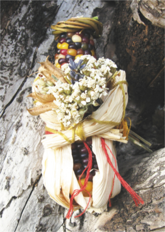 small spirit doll made from decorative corn, holding a bouquet of dried yarrow and lavender flowers