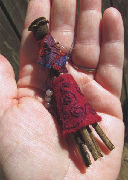 small spirit doll made of twigs and rosehips, with red and purple embroidered clothes, adorned with round beads