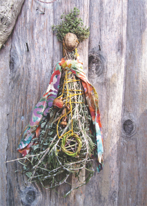 spirit doll made of dried herbs tied together with yellow thread, adorned with colorful fabric, rose hips, and a miniature pentacle wreath