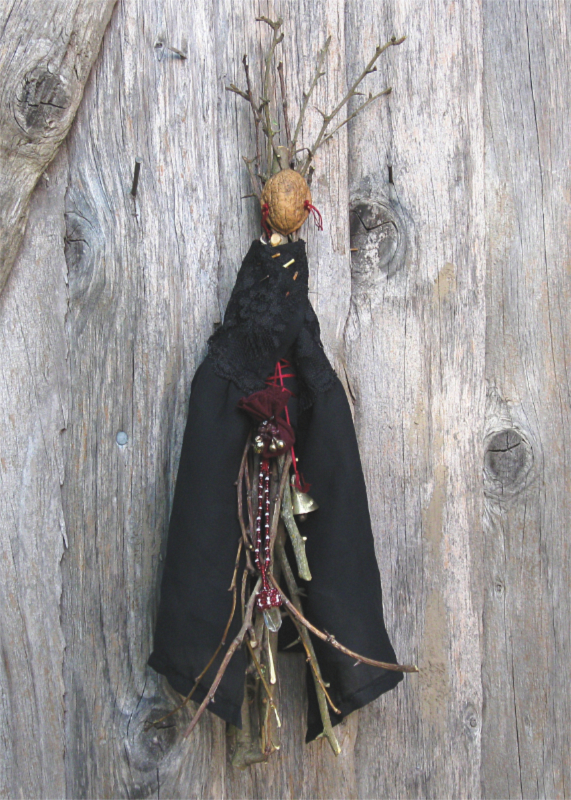 doll made of hawthron twigs with an empty walnut shell for a face, wearing a black cape held closed with thorns