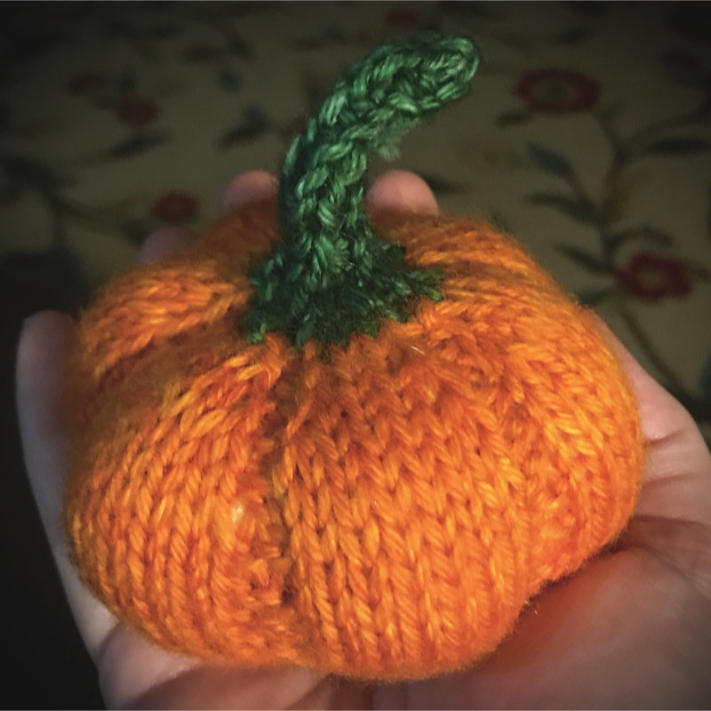 palm sized knitted pumpkin with bright orange body and green stem