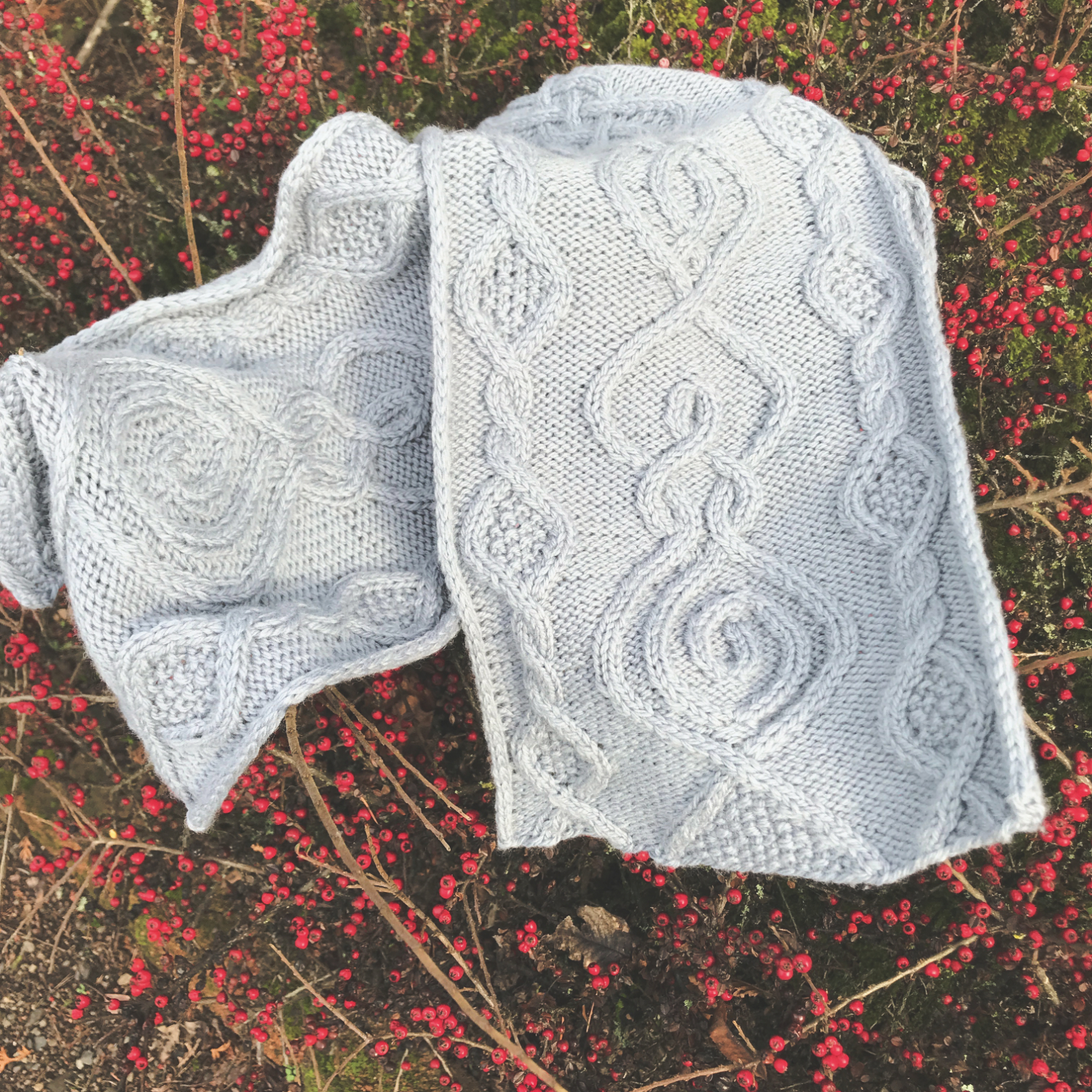 a grey cable knit scarf with a goddess motif on a background of red berries