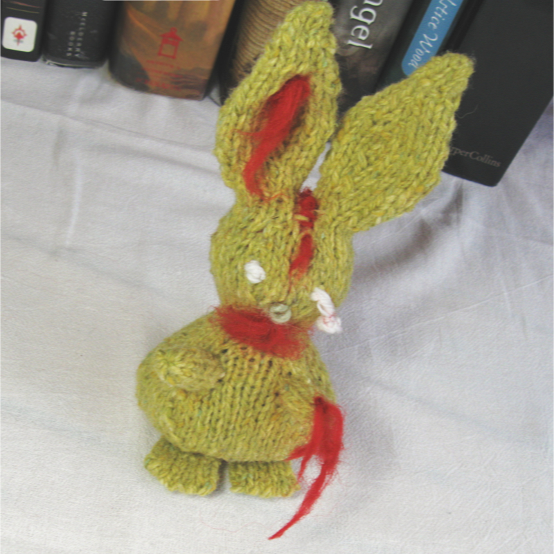 greenish yellow knitted zombie bunny with one dangling eyeball and red "blood" made of wool roving