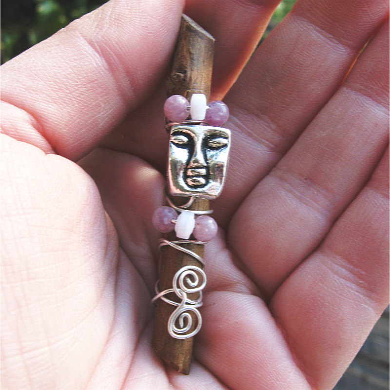 a piece of a rose stem adorned with silver wire, rose quartz and lepidolite beads, and a tranquil face with closed eyes.