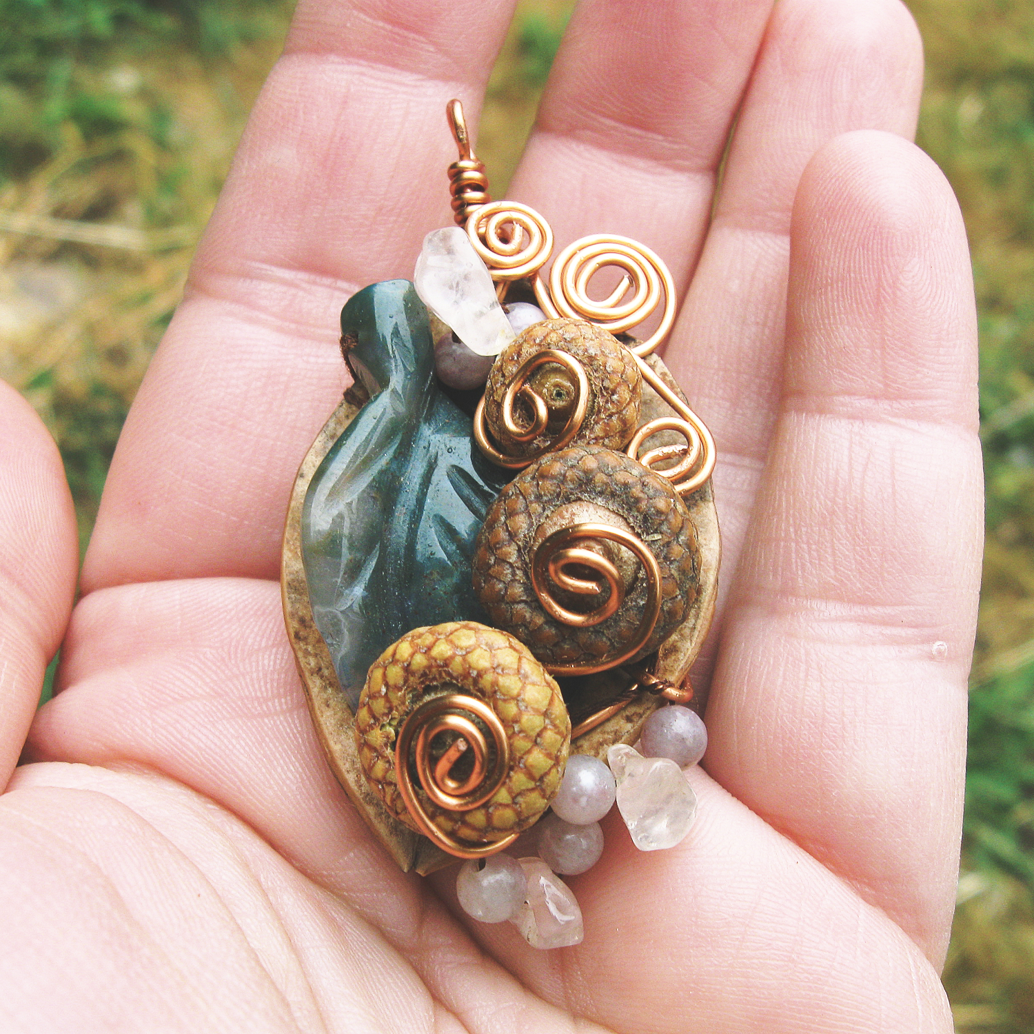 half a walnut shell adorned with tiny acorns, rose quartz beads, and a green leaf bead, with copper wire spirals