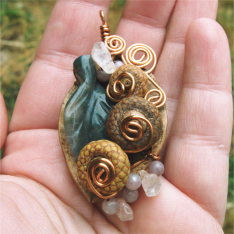 half a walnut shell adorned with tiny acorns, rose quartz beads, and a green leaf bead, with copper wire spirals