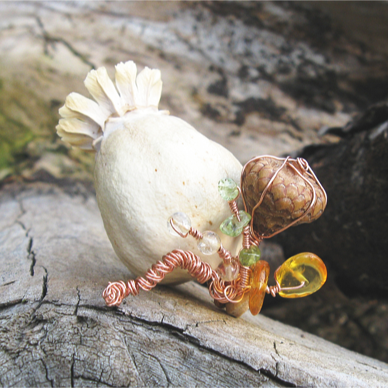 white poppy pod adorned with copper wire, amber, peridot, and a small acorn