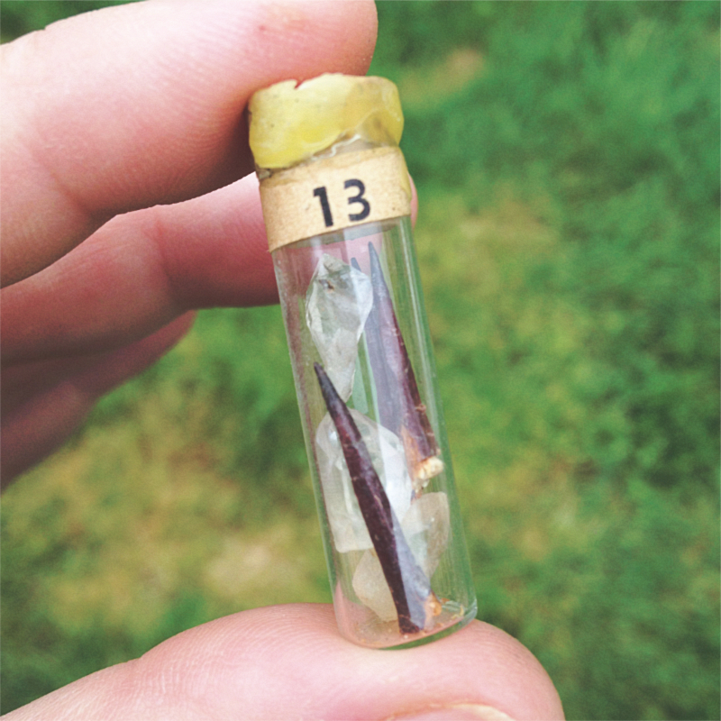 tiny glass vial with two thorns and three pieces of clear quartz, with a label that reads "13", sealed with a cork and beeswax