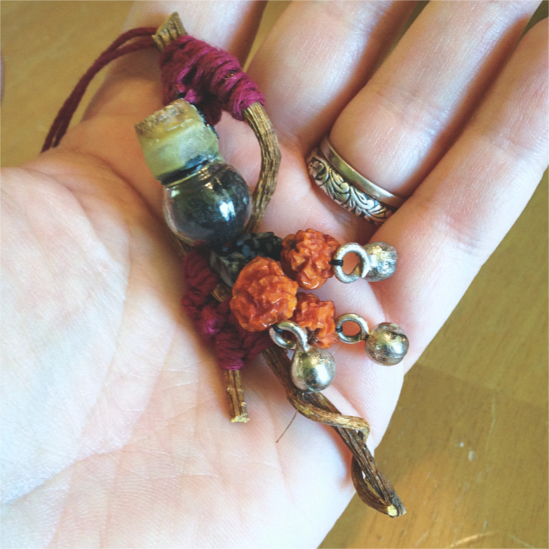 twisty roots woven together with red thread, adorned with a tiny round jar of black salt, rosehips, and small silver bells