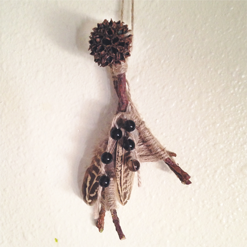 twigs woven together with twine, adorned with a sweet gum pod, feathers, and smoky quartz beads