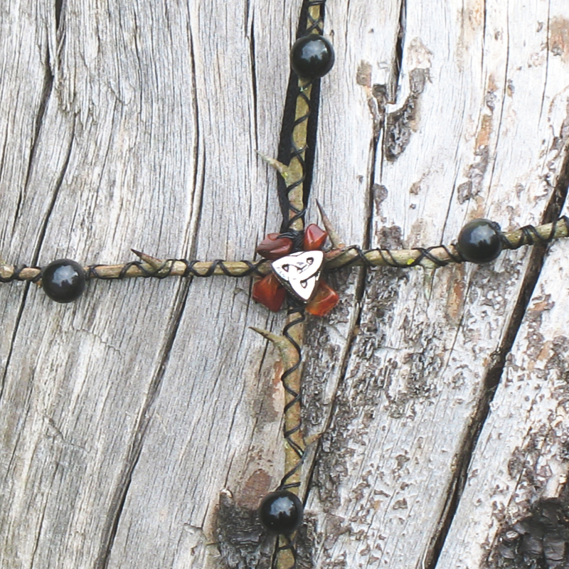 equal armed cross of hawthorn twigs embellished with black thread, smoky quartz, carnelian, and a silver triquetra charm