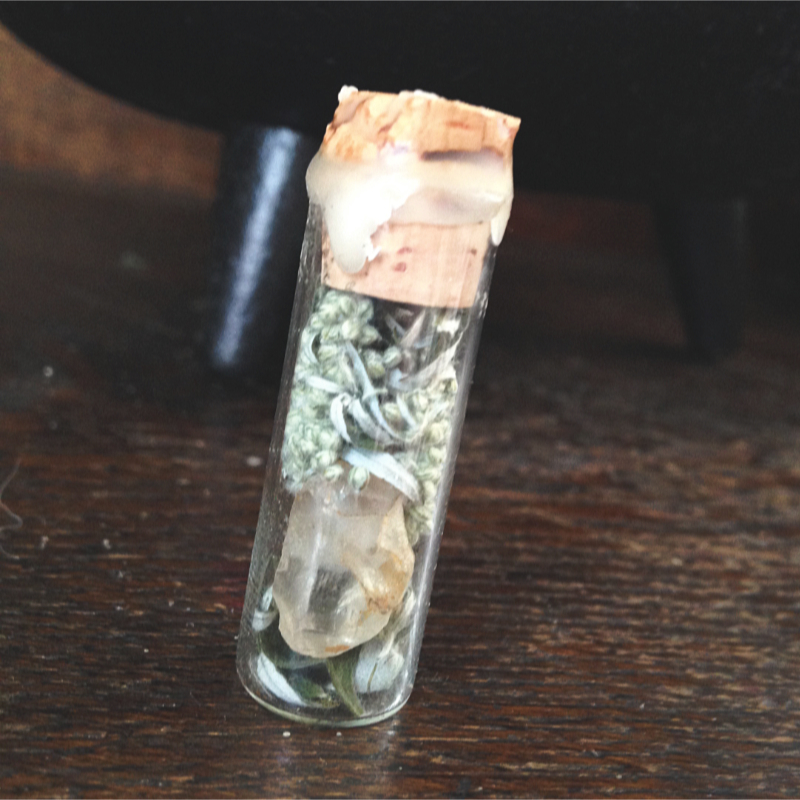 a tiny jar filled with mugwort and raw quartz crystals, sealed with a cork and beeswax
