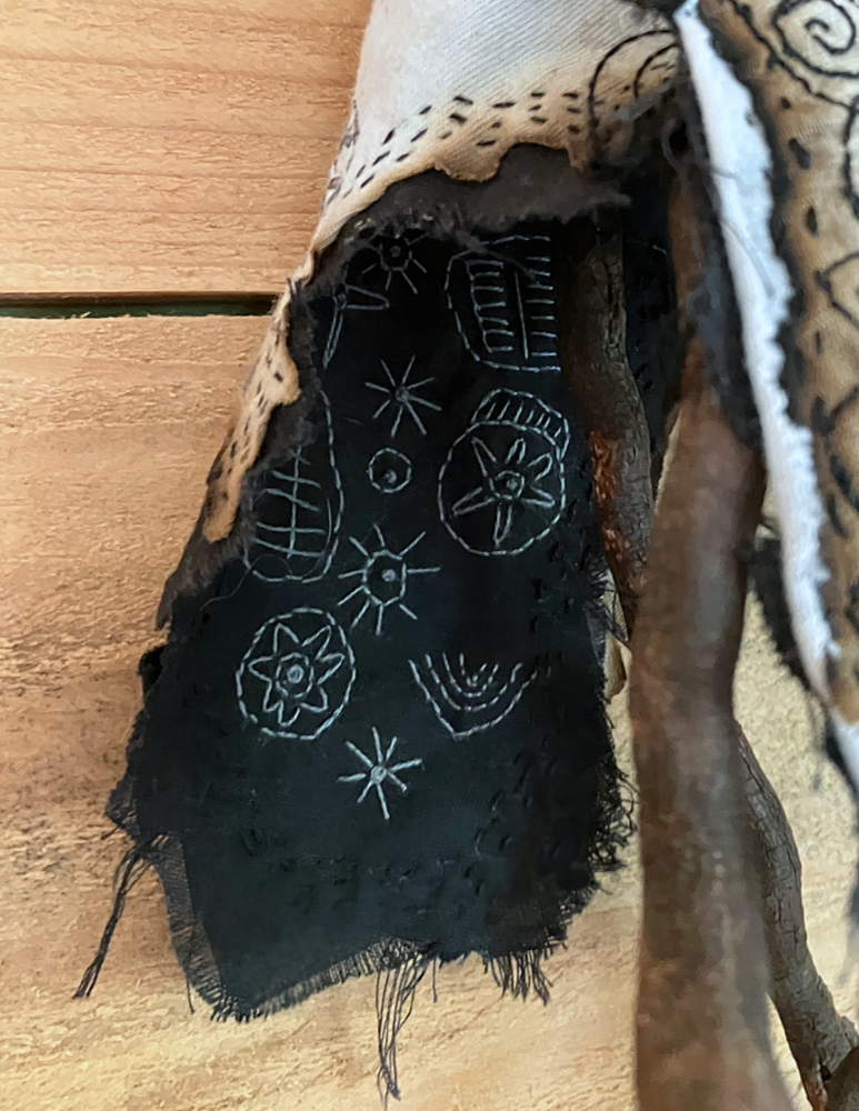 Closeup of gray stitching on black fabric. The stitching depicts symbols inspired by megalithic carvings in stone at The Mountain of the Cailleach.