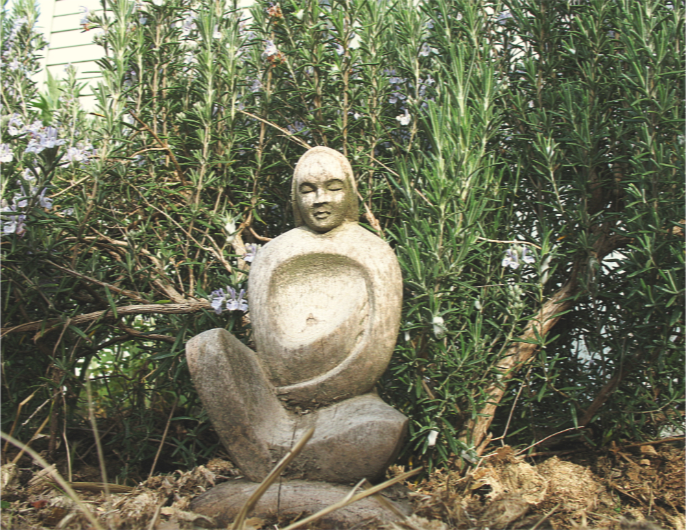 a wooden statue of a woman in front of a rosemary bush