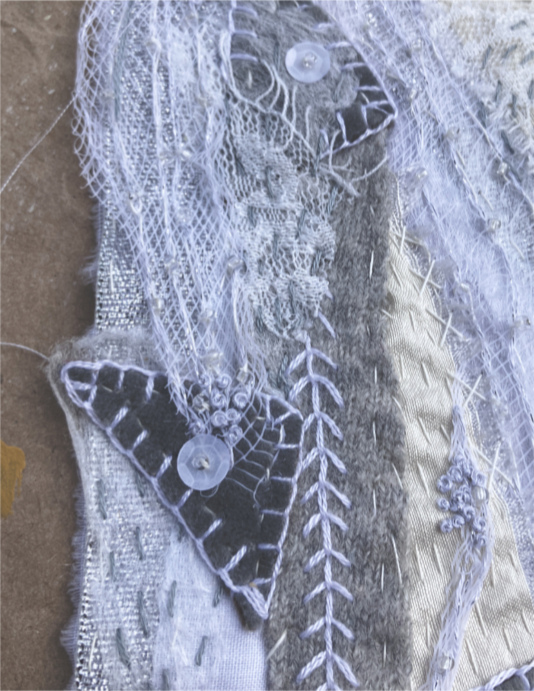 detail of a fabric collage in shades of white and gray with hand stitching, beads, sequins, and buttons
