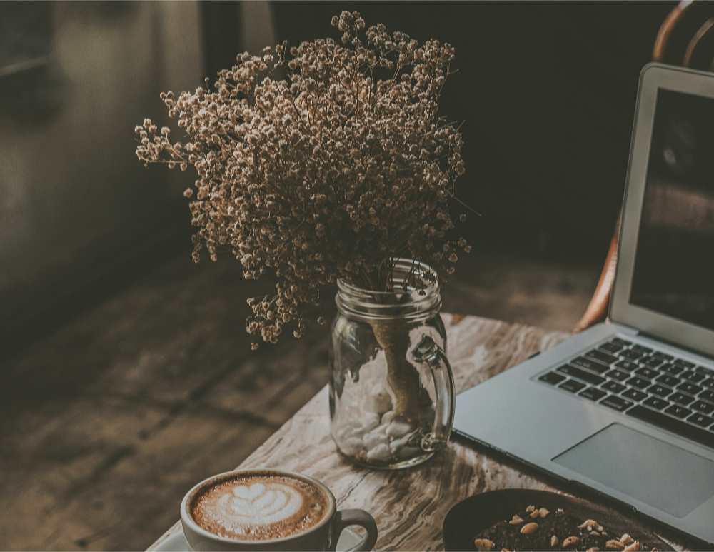 a jar of dried flowers and a cup of coffee beside a laptop