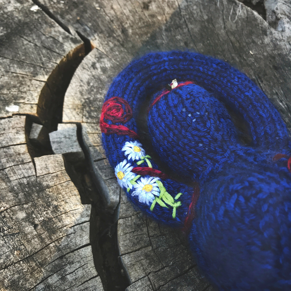 closeup of daisies embroidered on the arm of a knitted goddess