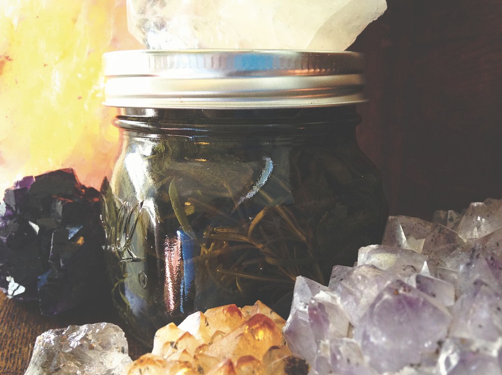 a mason jar filled with herbs and water surrounded by crystals