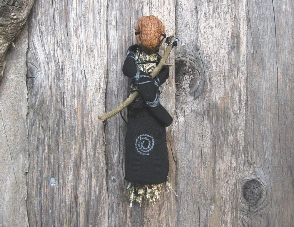 an art doll with a walnut face and black embroidered clothing