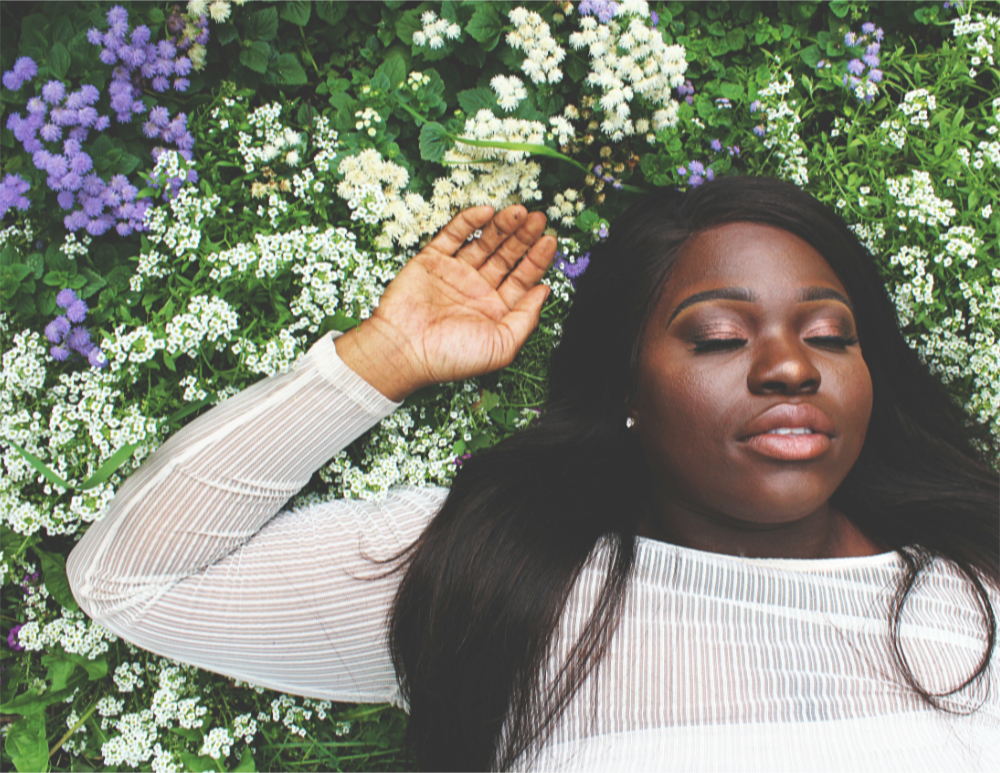a woman in a white shirt sleeps on a bed of white and purple flowers