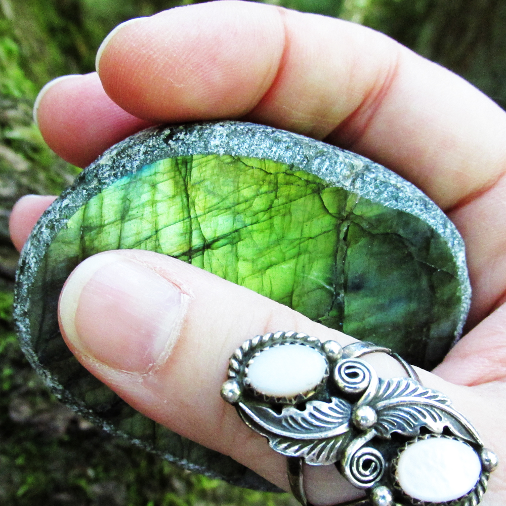 a hand holding an labradorie stone, wearing an ornate ring