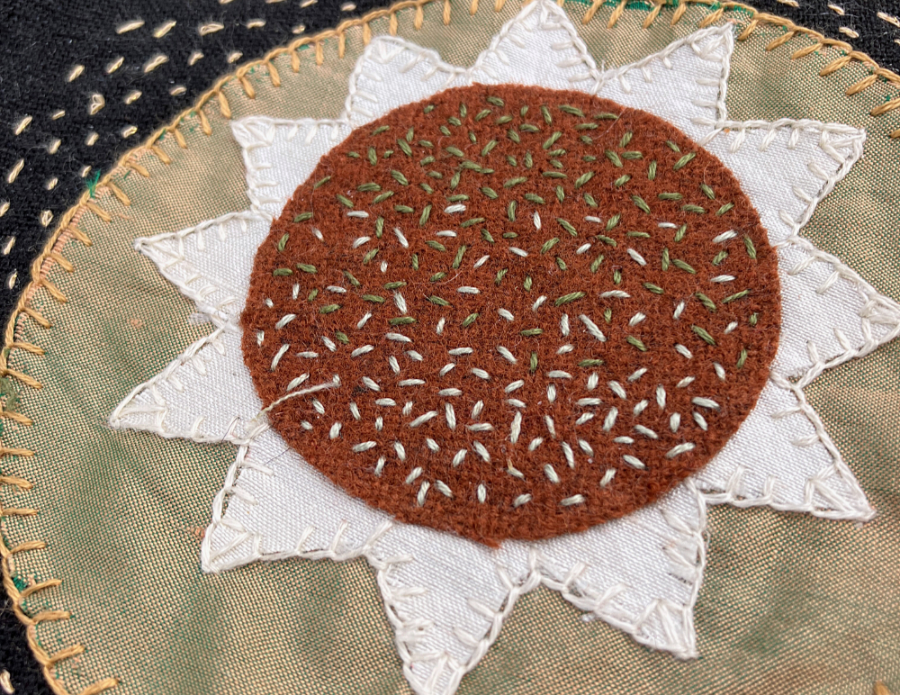 A close up of seed stitch on a circle of rust-brown wool