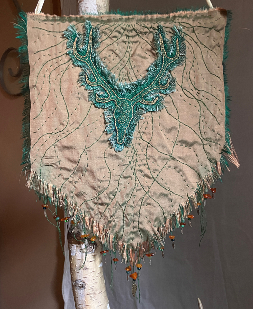 A green woven fabric embroidered with an antlered stag head on a gold silk background