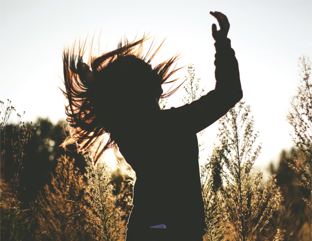 Silhouette of a person with long hair dancing in a field of wild plants