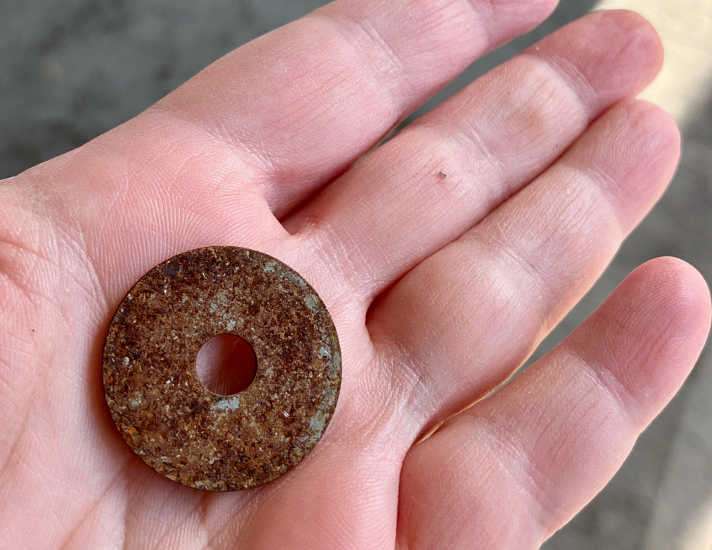 A human hand holding a rusty washer