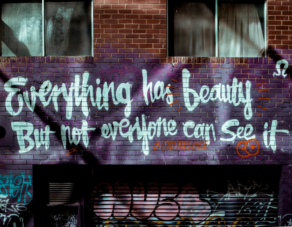 An apartment building wall with graffiti that reads "Everything has beauty, but n ot everyone can see it"
