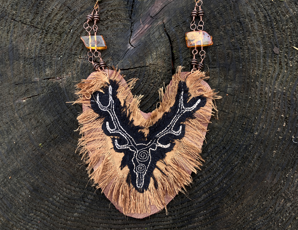 Closeup of an embroidered stag on bronze silk with a fringe of frayed edges.