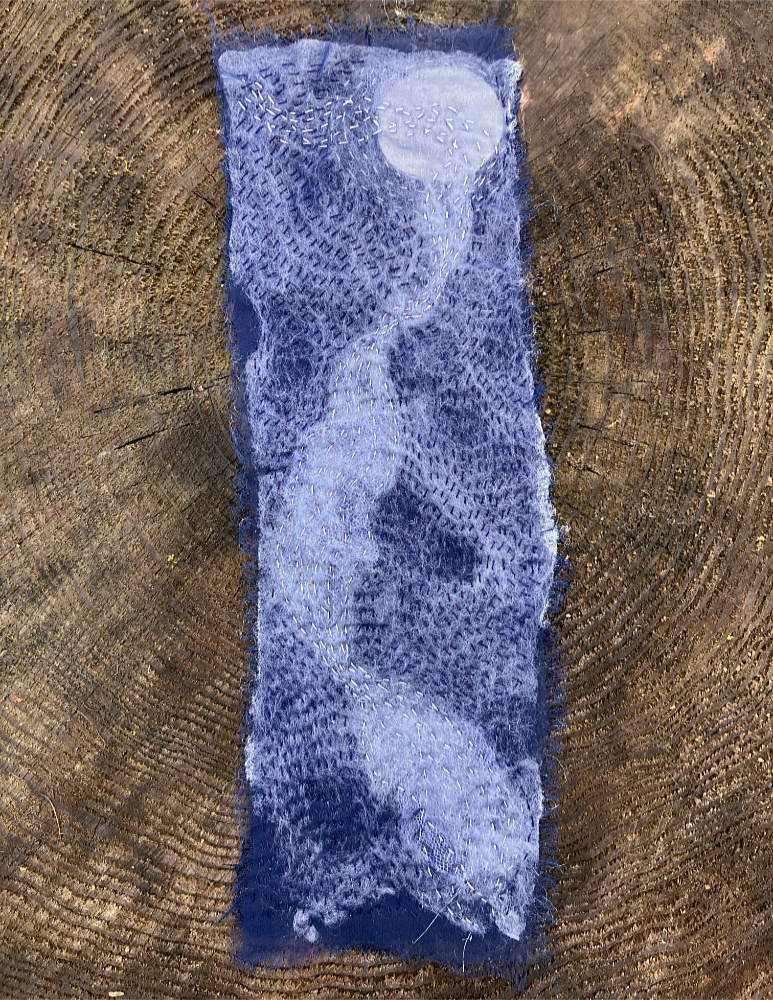A blue and white rectangle of fabric with dark blue, white, and silver stitching, creating a stylized representation of moonlight on moving water